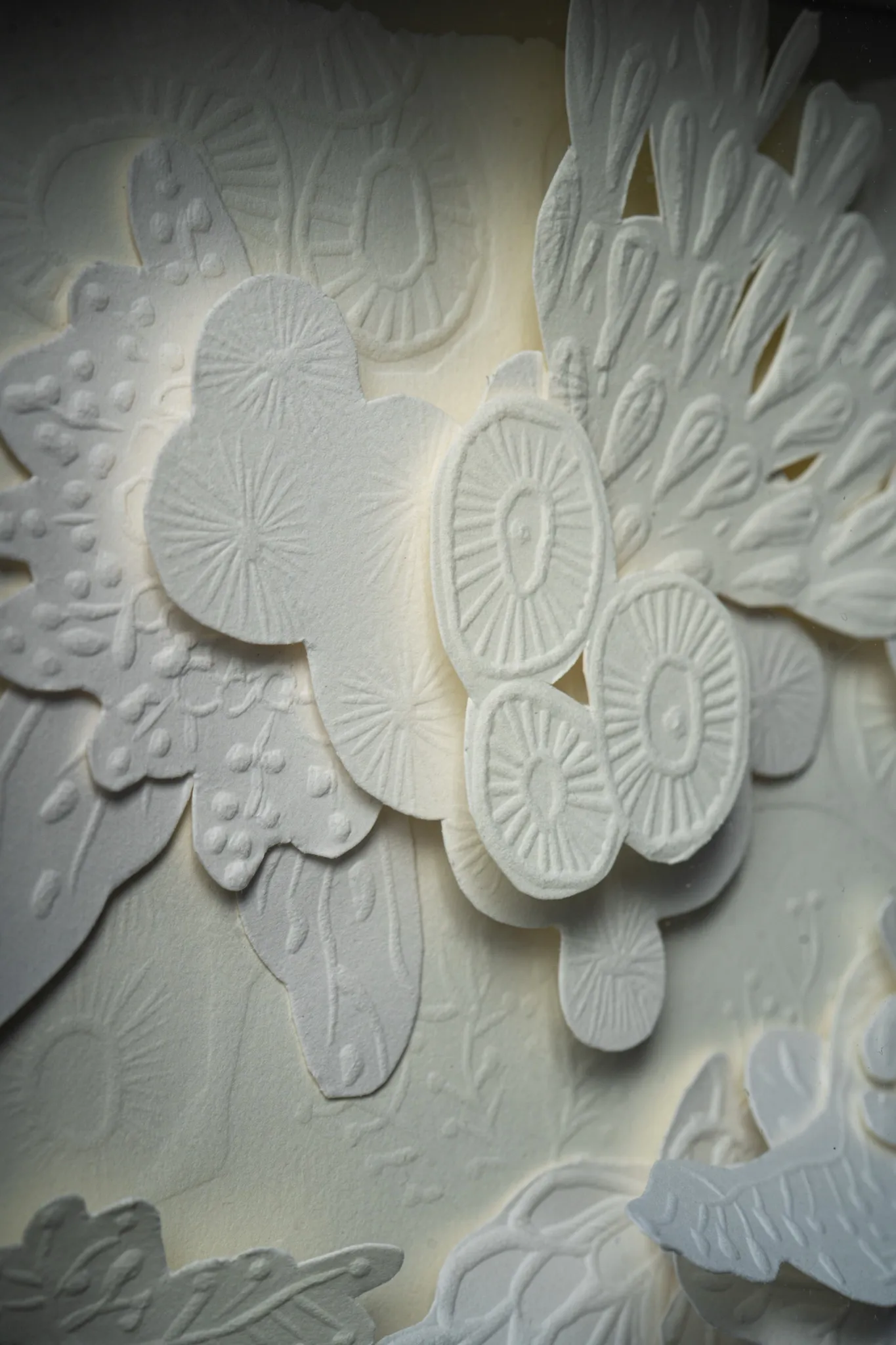 Detail of Mar Blanco. Raised discs with radiating embossed lines stack over a dotted leaf shape and a fan of pointed petals.