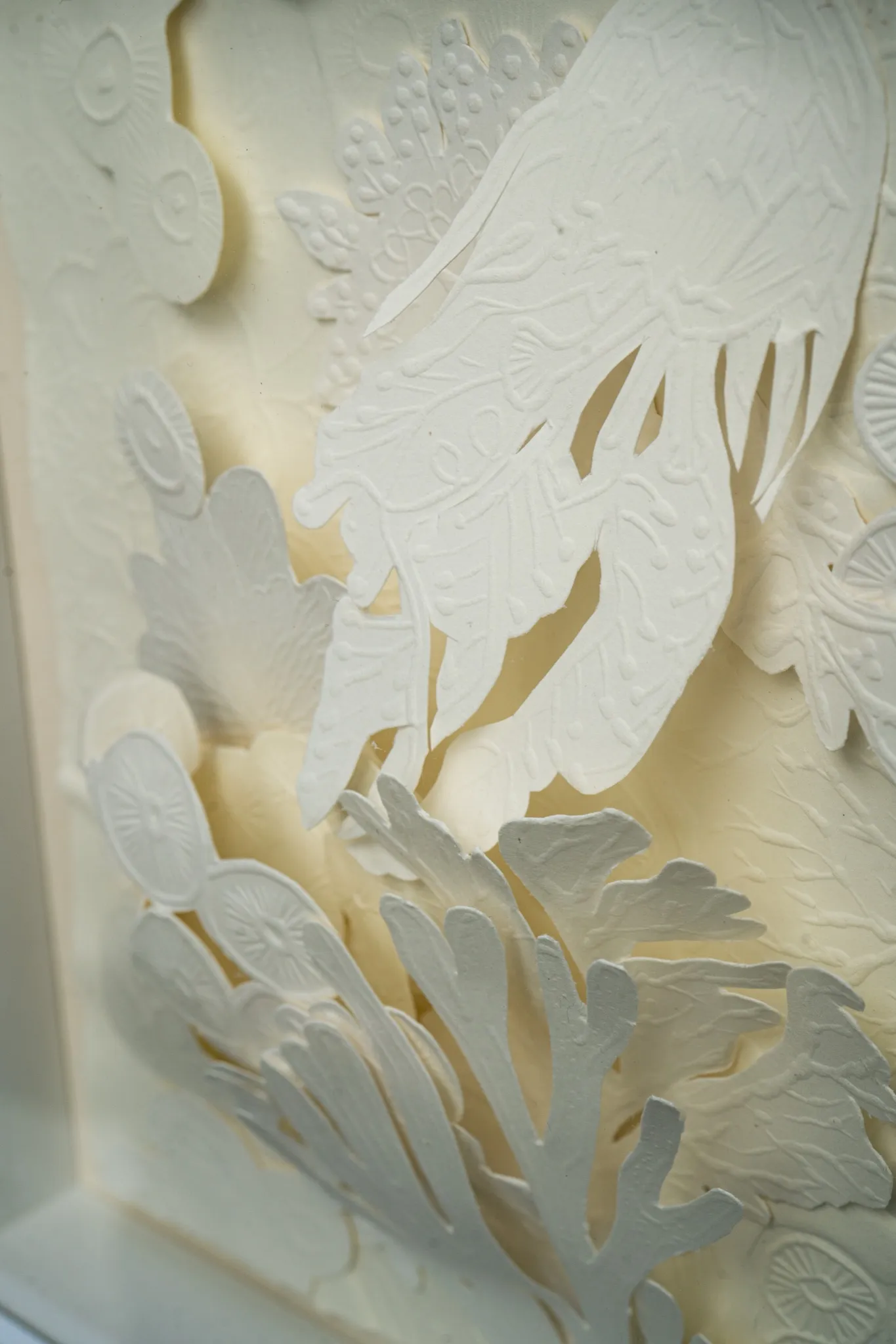Angled detail of Mar de Kara. A cut coral branch and embossed discs stand off the sheet beneath the trailing tentacles of the jellyfish form.