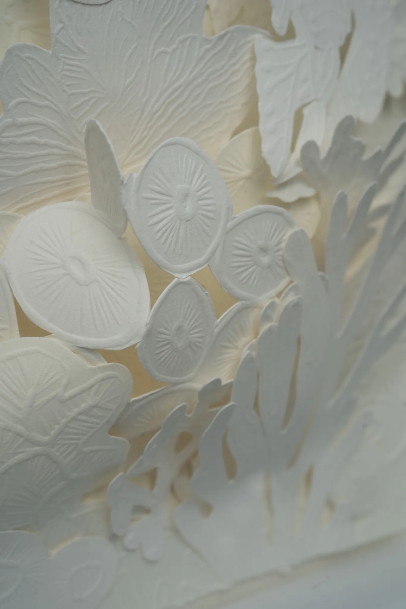 Close detail of Mar de Kara. Overlapping embossed discs and a ribbed shell shape sit at the foot of the cut coral branch.