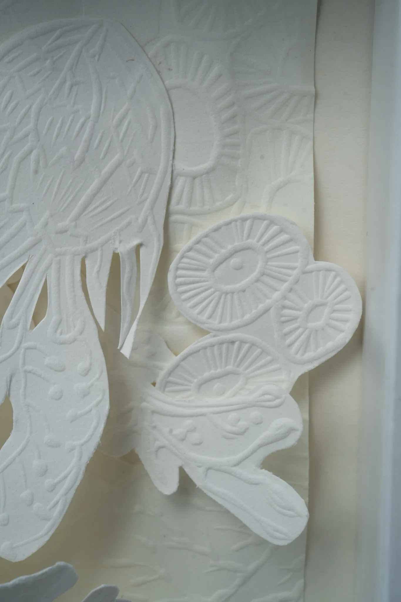 Detail at the edge of Mar de Kara. A pair of embossed discs and the tentacles of the jellyfish form lie over creased paper beside the inside of the frame.